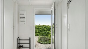 Un couloir avec un meuble à chaussures, un tableau électrique et une porte donnant sur un jardin.
