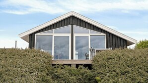 Un bâtiment moderne doté de grandes fenêtres, d’une terrasse en bois et surplombant un ciel dégagé.