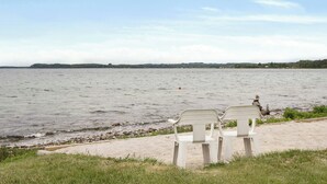 Une plage avec deux chaises en plastique blanches, placées face à la mer, un sentier de sable et une côte lointaine bordée de végétation.