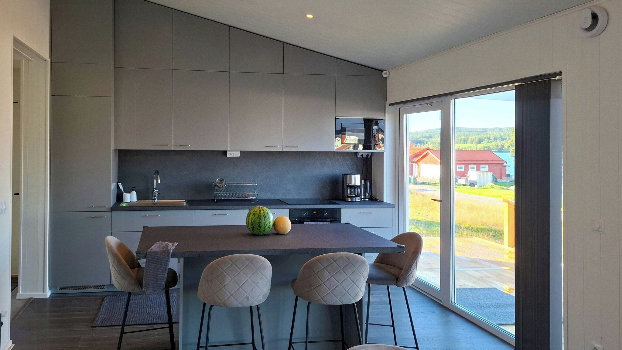 A modern kitchen with a central island, bar stools, and a large window offering a view of the outdoors.