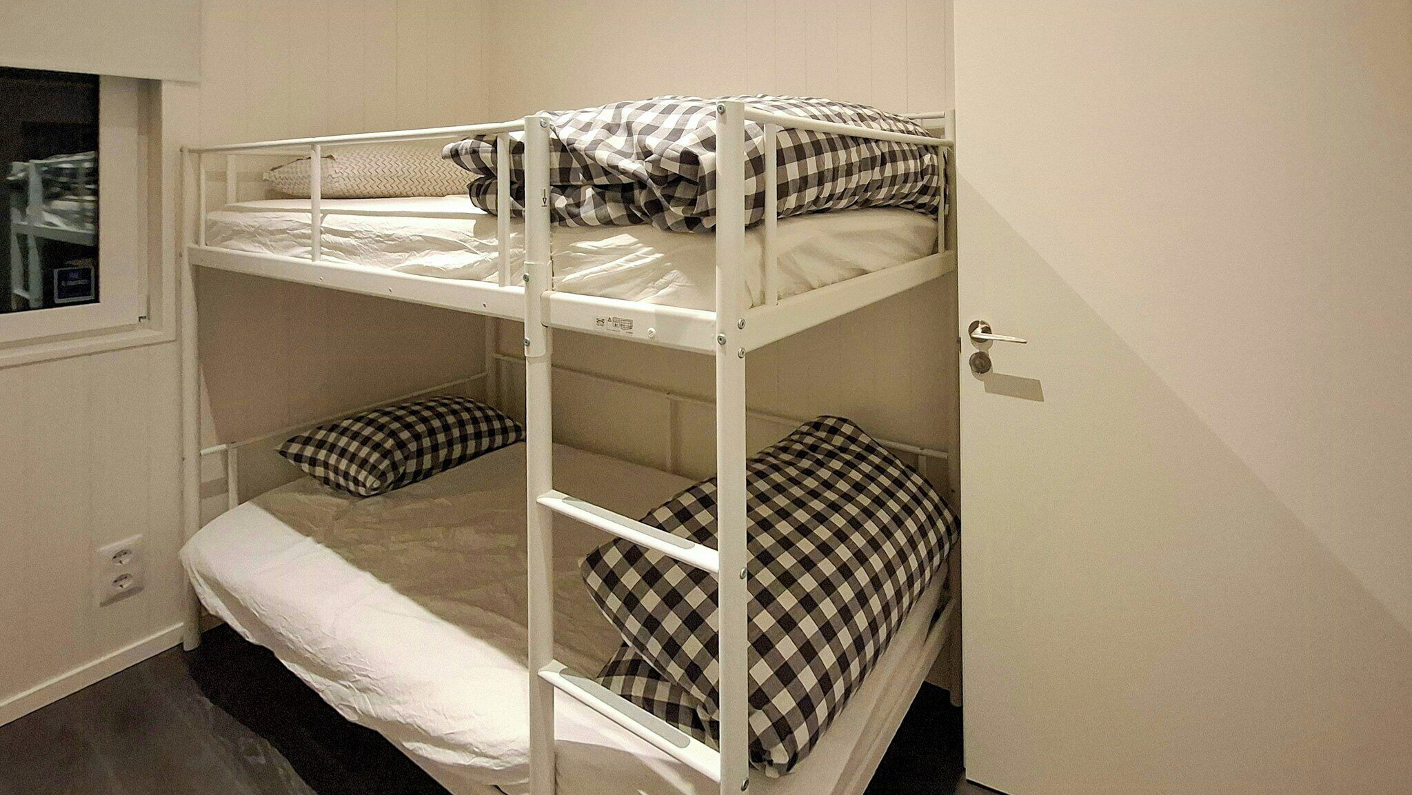 A bunk bed room with white metal railings, checkered bedding, and a window.