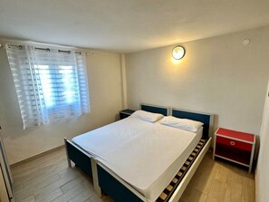Ein Schlafzimmer mit einem Bett, Nachttischen, einem Fenster mit Vorhängen und einer roten Kommode.