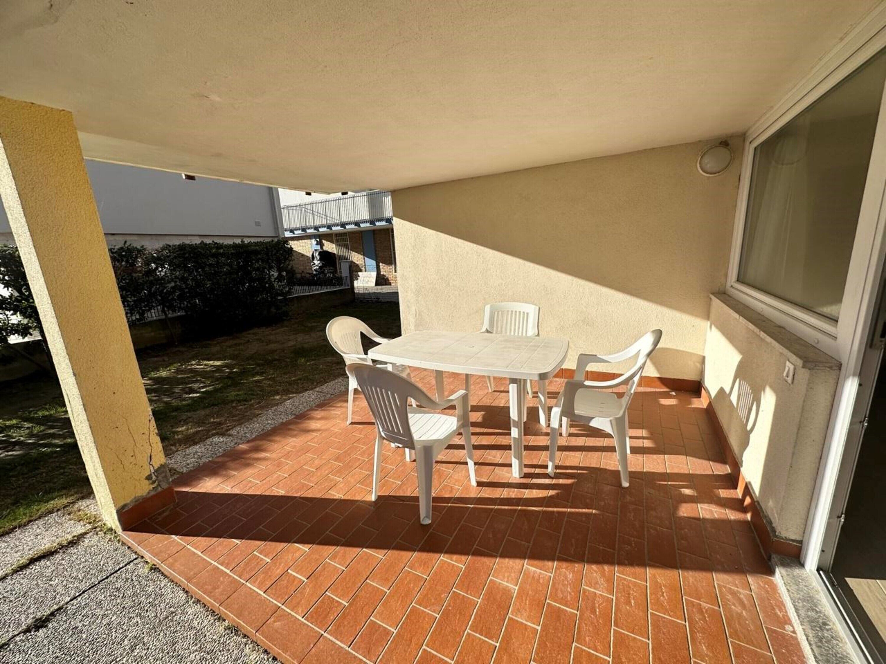 An outdoor patio with a table and chairs, a tiled floor, and a view of a building in the background.