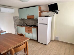 Eine kompakte Küche mit Essbereich, einer eingebauten Kochplatte, einem Kühlschrank und einem montierten Fernseher.