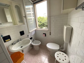 Et badeværelse med vask, toilet, bidet og et vindue.