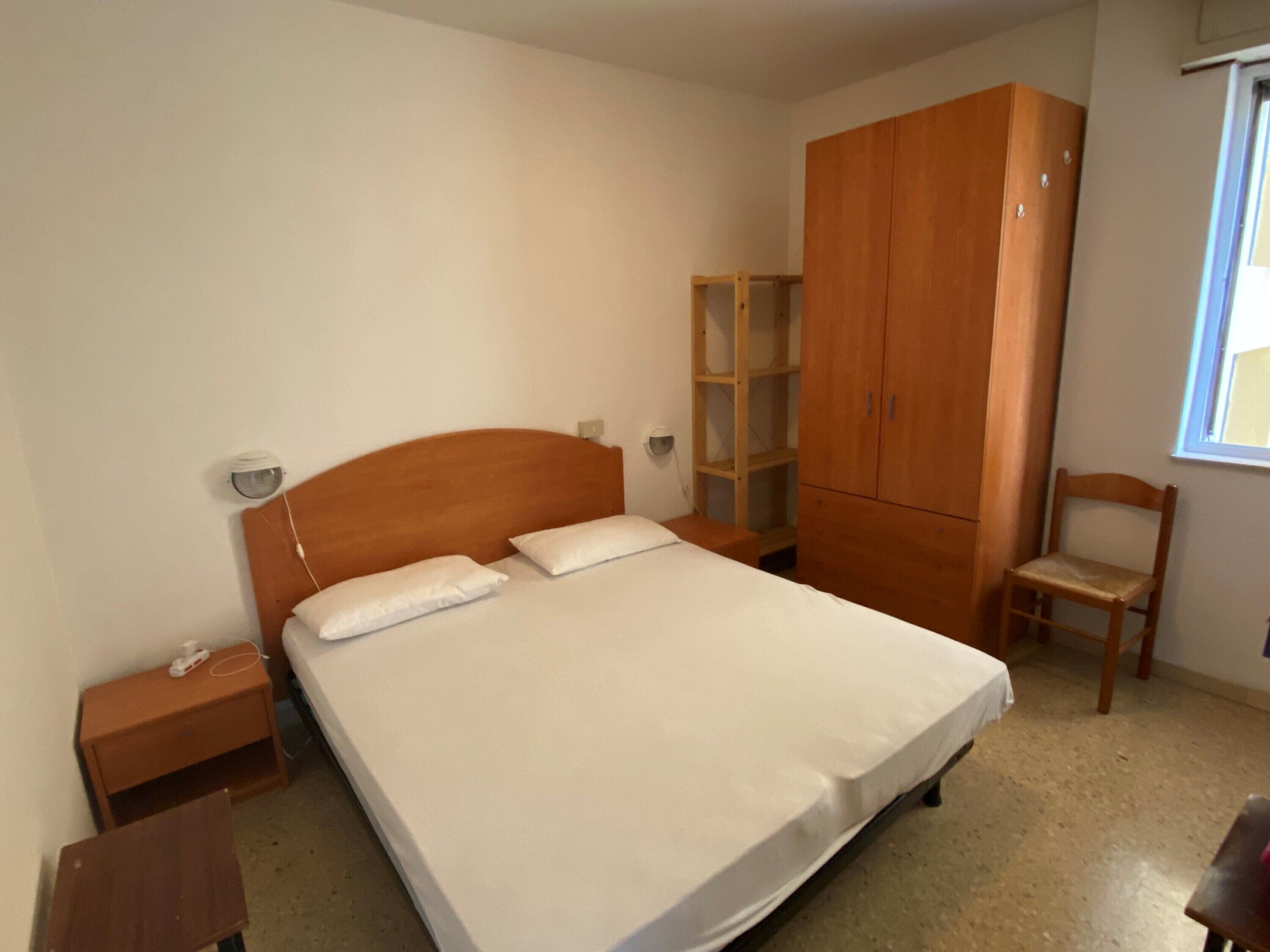 Un dormitorio con cama, armario de madera, mesita de noche y una silla.
