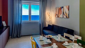 Un comedor con una mesa lista para cuatro personas, un sofá y una ventana con vista al mar.
