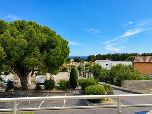 Ein Wohngebiet mit einem großen Baum, parkenden Autos und Gebäuden mit Blick auf das Meer.