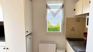 Eine kleine Küche mit Fenster, weißen Schränken, einer Heizung und einem Mülleimer.