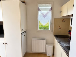 Eine kleine Küche mit Fenster, weißen Schränken, einer Heizung und einem Mülleimer.