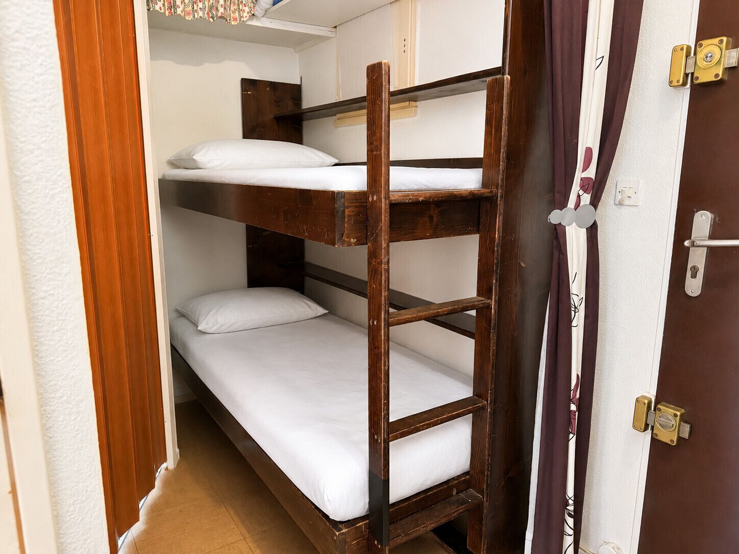 Una cama individual con ropa blanca, cabecera de madera y una puerta con cerradura.