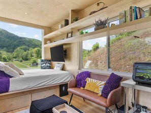 Un espacio habitable compacto con cama, sofá, televisión y ventana con vistas a un paisaje verde.