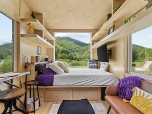 Ein gemütliches Schlafzimmer mit Bett, Schreibtisch und Fenster mit Blick auf eine bewaldete Landschaft.
