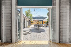 Uma porta de correr de vidro dá para um alpendre externo com mesa e cadeiras, uma rede e um pergolado com luzes de corda.