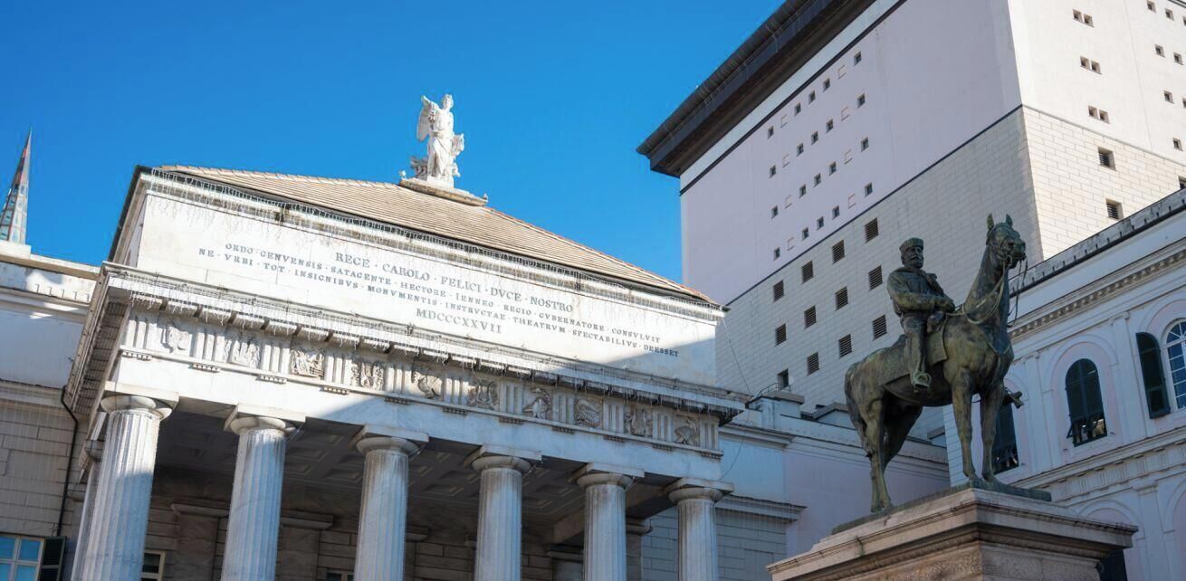 A classical building facade with columns, a statue, and an inscription.
