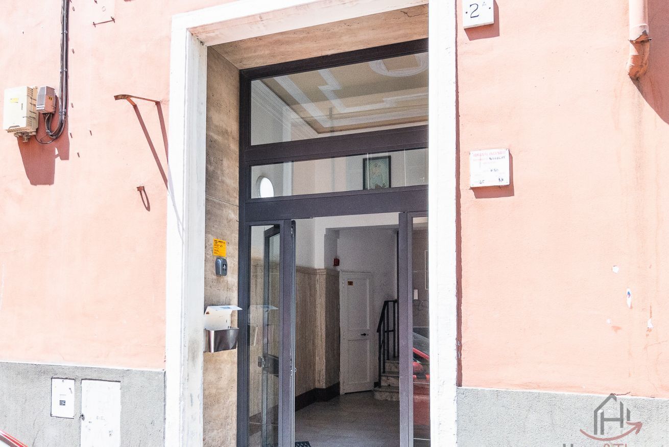 Une entrée d’immeuble avec une porte vitrée, un escalier et une enseigne fixée au mur.