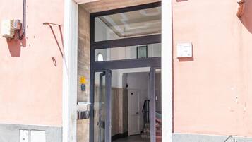Entrada de un edificio con puerta de cristal, una escalera y un cartel en la pared.
