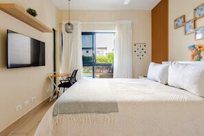Quarto de hotel com cama, televisão, secretária e vista para o exterior.