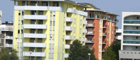 Un edificio de varios pisos con balcones, un área de piscina con sombrillas y un cielo despejado.