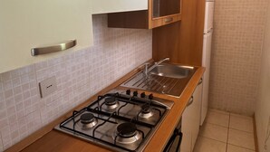 Cuina compacta amb fogó de gas, un rentapeus i armaris blancs.