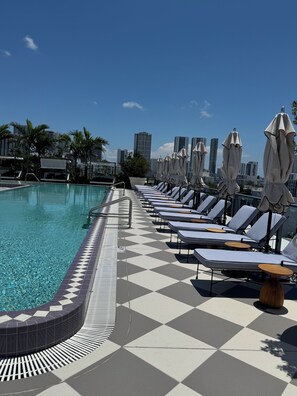 Ein Poolbereich mit Liegestühlen und Sonnenschirmen, ein gefliestes Deck und eine Skyline im Hintergrund.