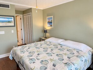 Ein Schlafzimmer mit einem Bett, einem Nachttisch, einer Lampe, einer Tür und einem gerahmten Bild an der Wand.