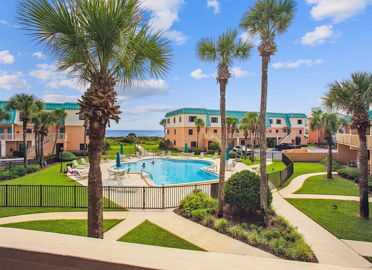 A resort with a swimming pool, palm trees, and a view of the ocean.