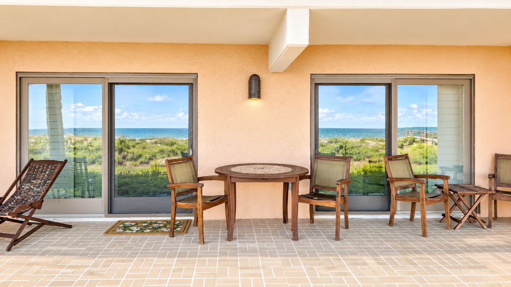 Un balcon avec une table et des chaises, de grandes fenêtres et une vue sur la verdure.