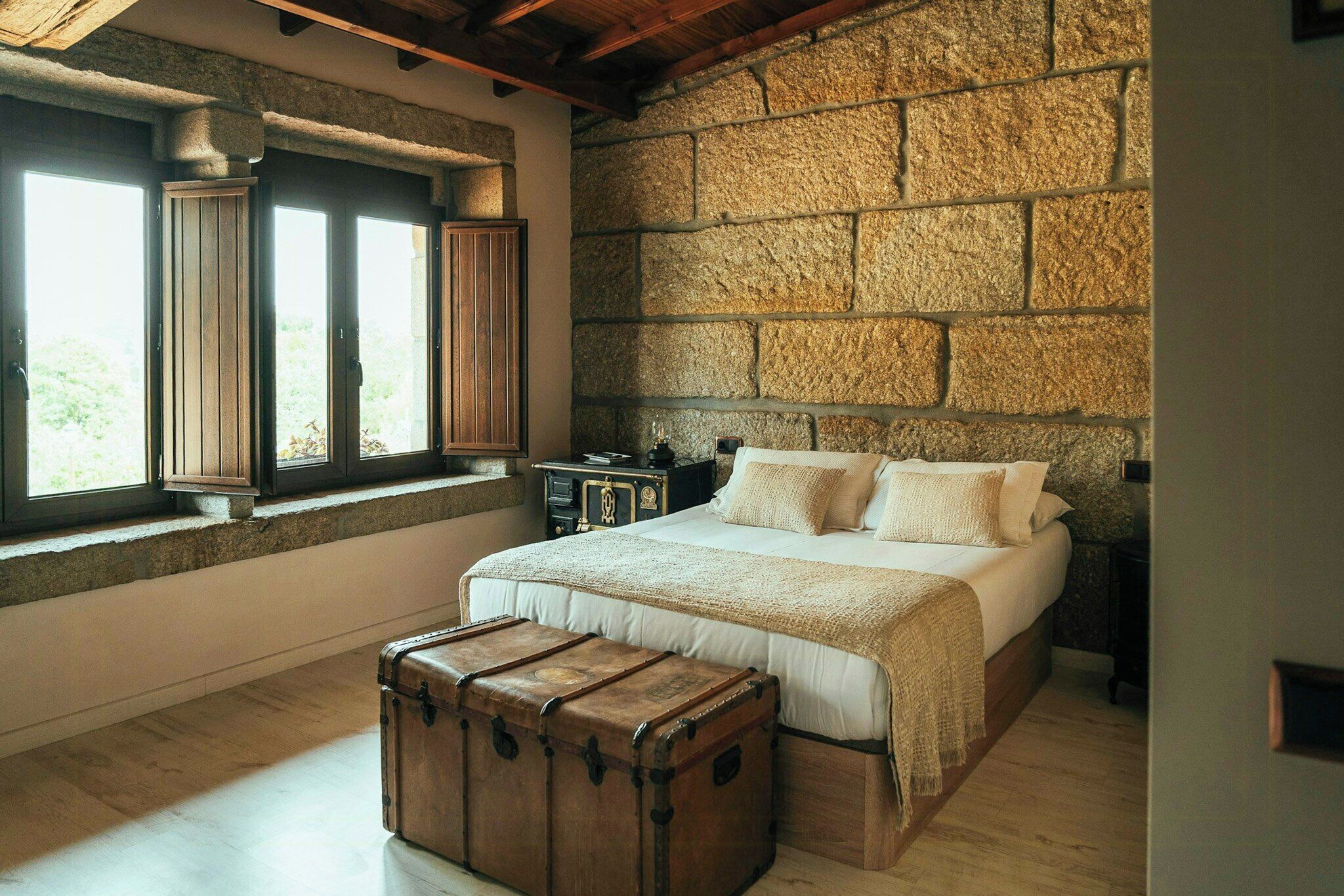 Une chambre avec un mur en pierre, un lit en bois et une vieille malle.