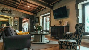 A cozy living room with a round coffee table, a sofa, a patterned armchair, and a television mounted on the wall. - Villa with private river in Vilagarcía, Galicia (Vilagarcia de Arousa)