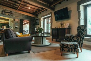 Een knusse woonkamer met een ronde salontafel, een bank, een fauteuil met een patroon en een televisie die aan de muur is bevestigd.