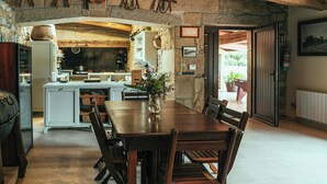 A rustic dining area with a wooden table and chairs, a stone wall, and a kitchen in the background. - Villa with private river in Vilagarcía, Galicia (Vilagarcia de Arousa)