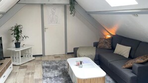 A loft-style room with a sloped ceiling, a white door with a simple line drawing, a grey sofa, a white coffee table, and a small white side table with a plant. - CENTRAL 55m2 - 4 PERSONNES - COSY - PROCHE NAUSICAA (Boulogne-sur-Mer)