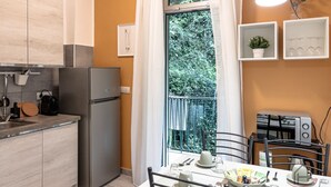 Eine kleine Küche mit Kühlschrank, Esstisch, Stühlen und einem Fenster mit Blick auf Grünflächen.