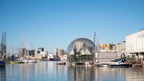 Ein Yachthafen mit Booten, einer großen, transparenten Kuppelstruktur und Industriegebäuden im Hintergrund.