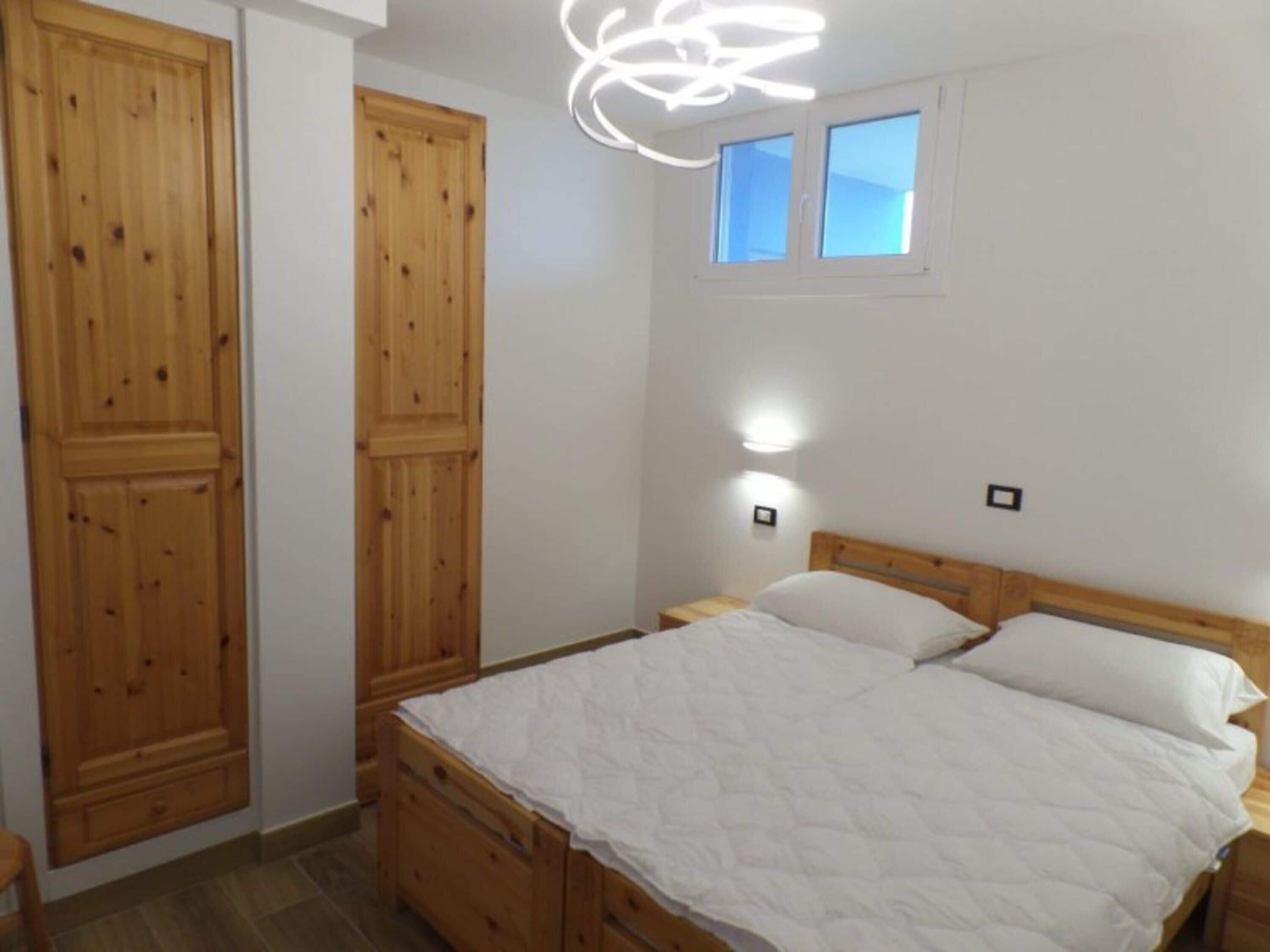 Un dormitorio con una cama de madera, una mesita de noche, un armario y una ventana pequeña.