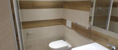A bathroom with a glass shower enclosure, a toilet, and a sink with a mirror above it.