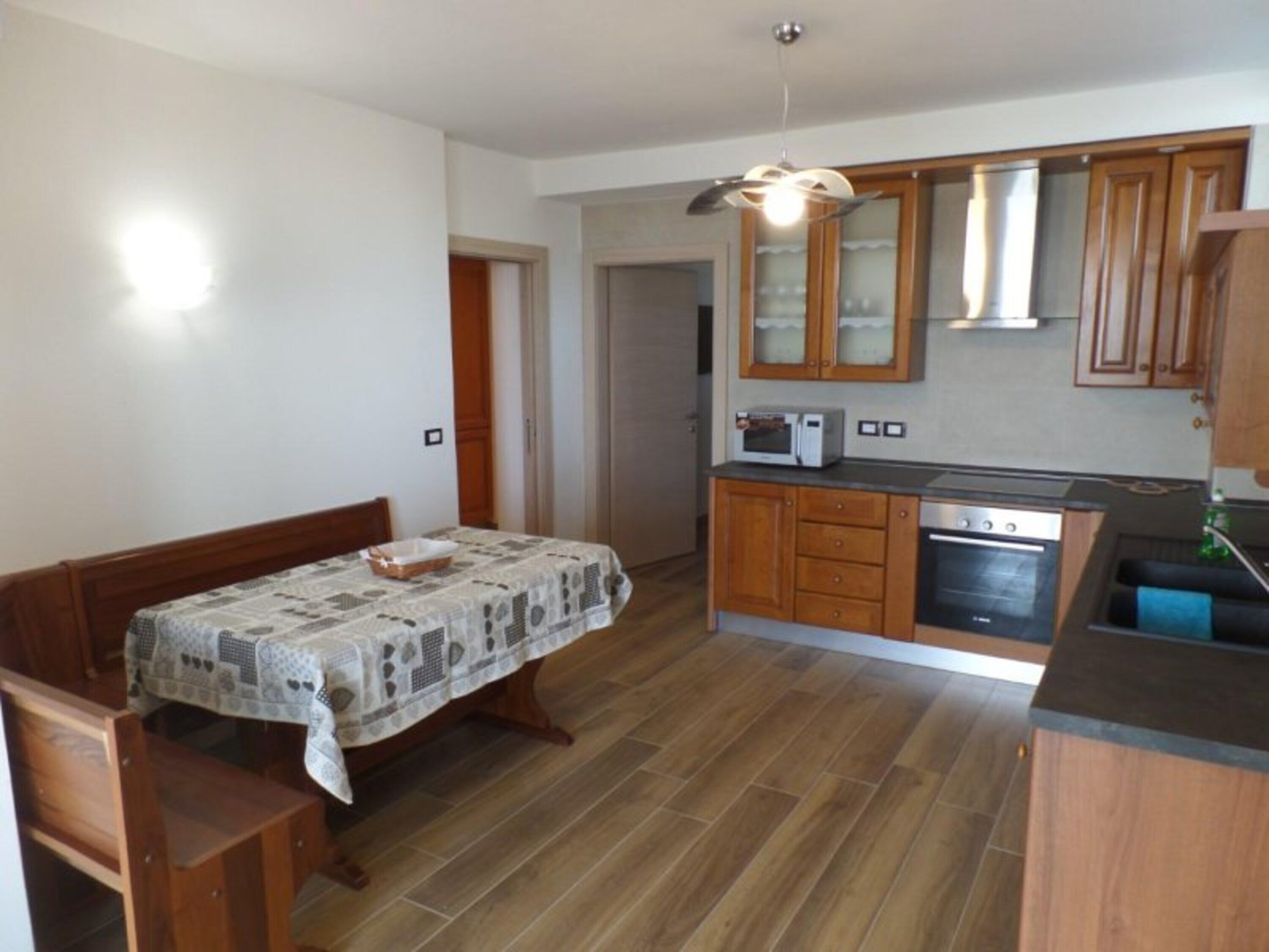 A compact kitchen with wooden cabinets, a microwave, an oven, and a dining area with a table and benches.