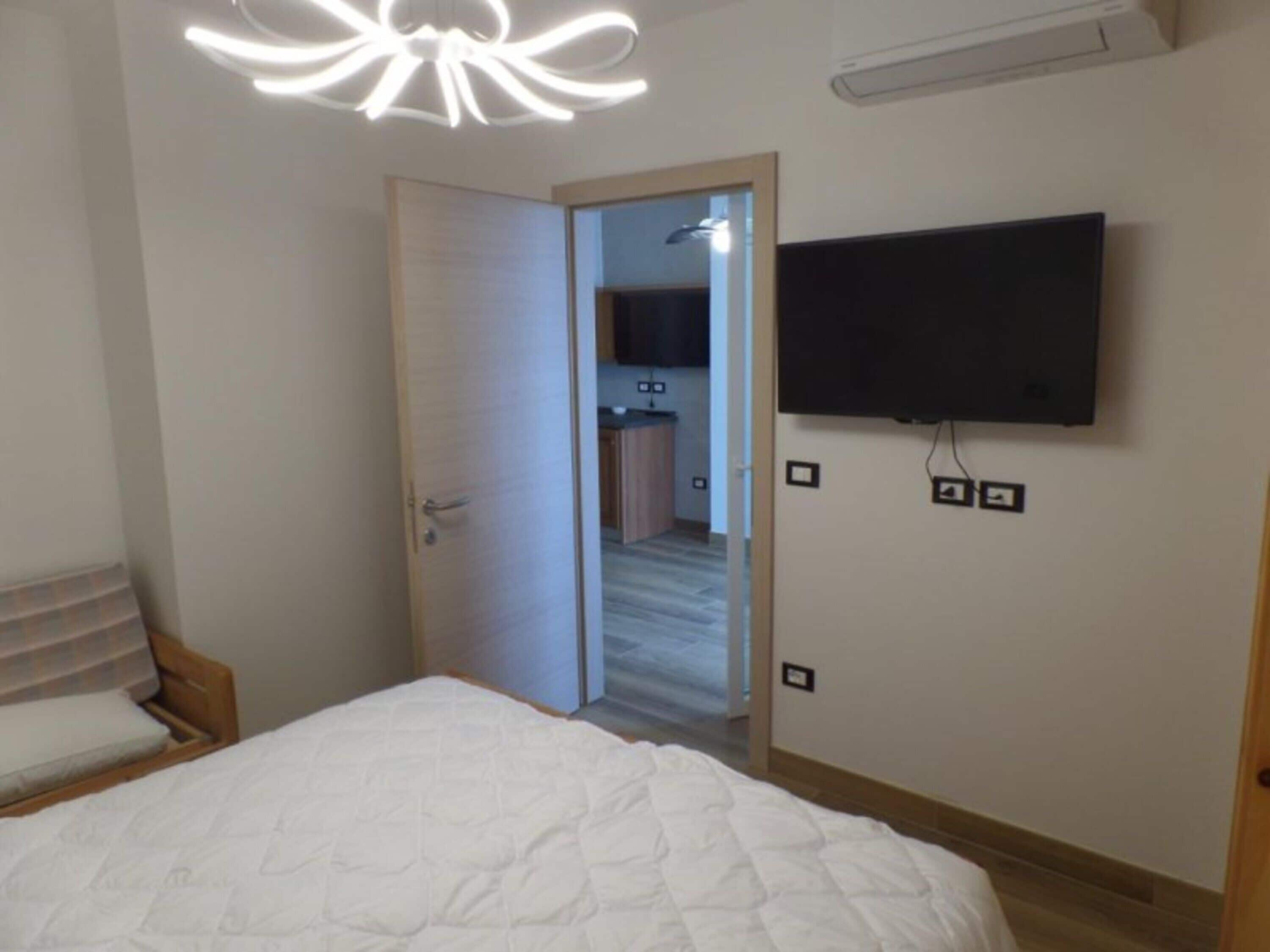 A bedroom with a bed, a TV mounted on the wall, and a door leading to a bathroom.