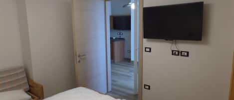 A bedroom with a bed, a TV mounted on the wall, and a door leading to a bathroom.
