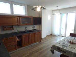 A kitchen with wooden cabinets, a black countertop, and a sink. There is a dining table with a tablecloth and a chair. - Seafront Flat With Splendid Views From the Terrace (San Michele al Tagliamento)