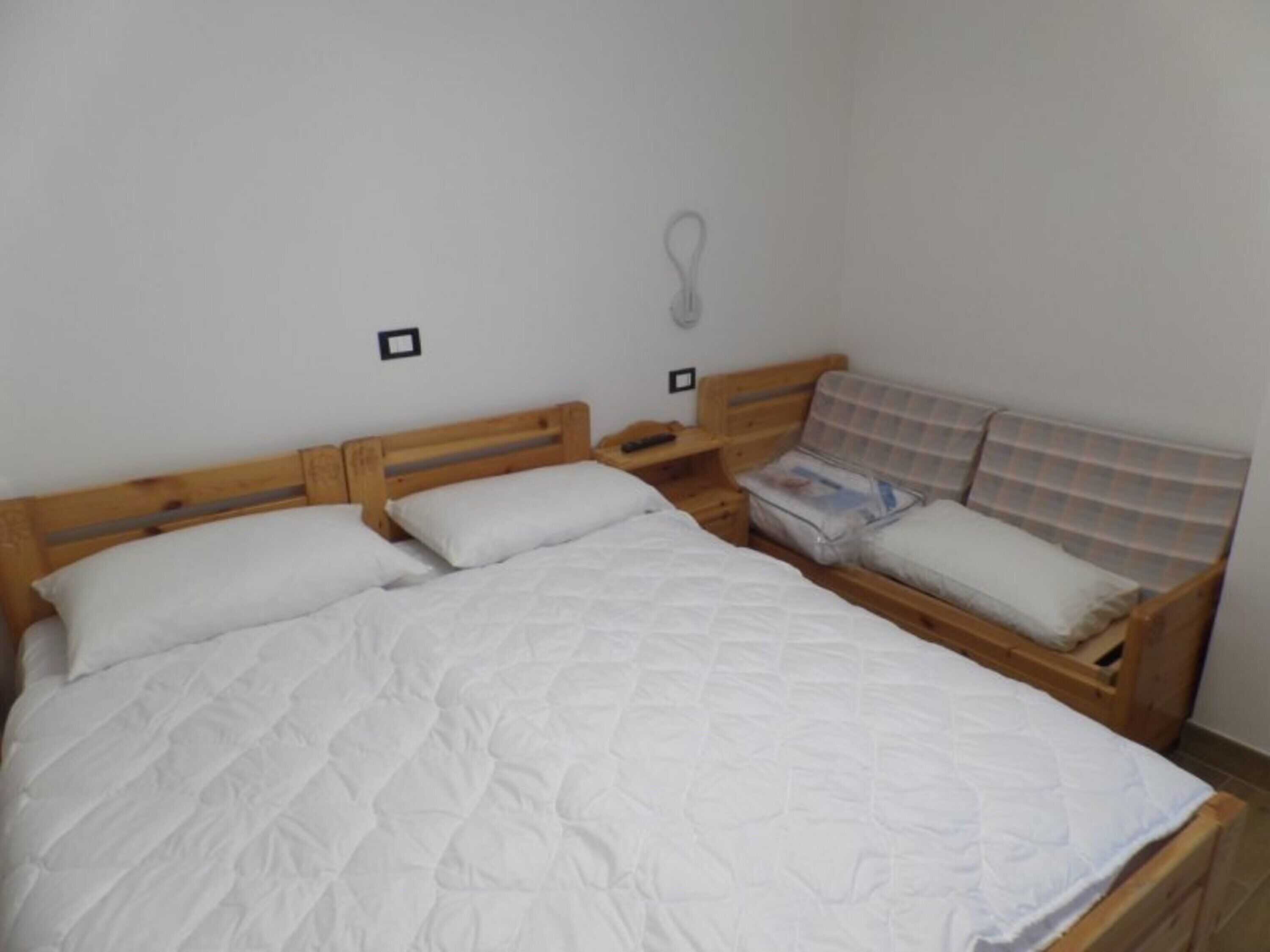 A room with a single bed, a wooden headboard, a nightstand, and a small seating area with a cushion.