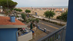 A balcony with a view of a beach, a street, and a building with a red roof. - Seafront Flat With Splendid Views From the Terrace (San Michele al Tagliamento)