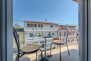 A balcony with two chairs and a table, a clear view of buildings in the background, and a metal railing.