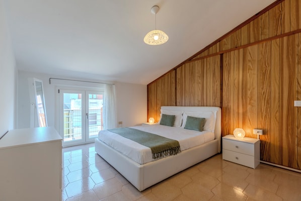 Ein Schlafzimmer mit Bett, Nachttischen, einem Kleiderschrank und einer Tür zum Balkon.