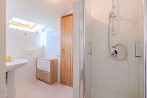 A modern bathroom with a glass shower enclosure, a wooden cabinet, and a white sink.