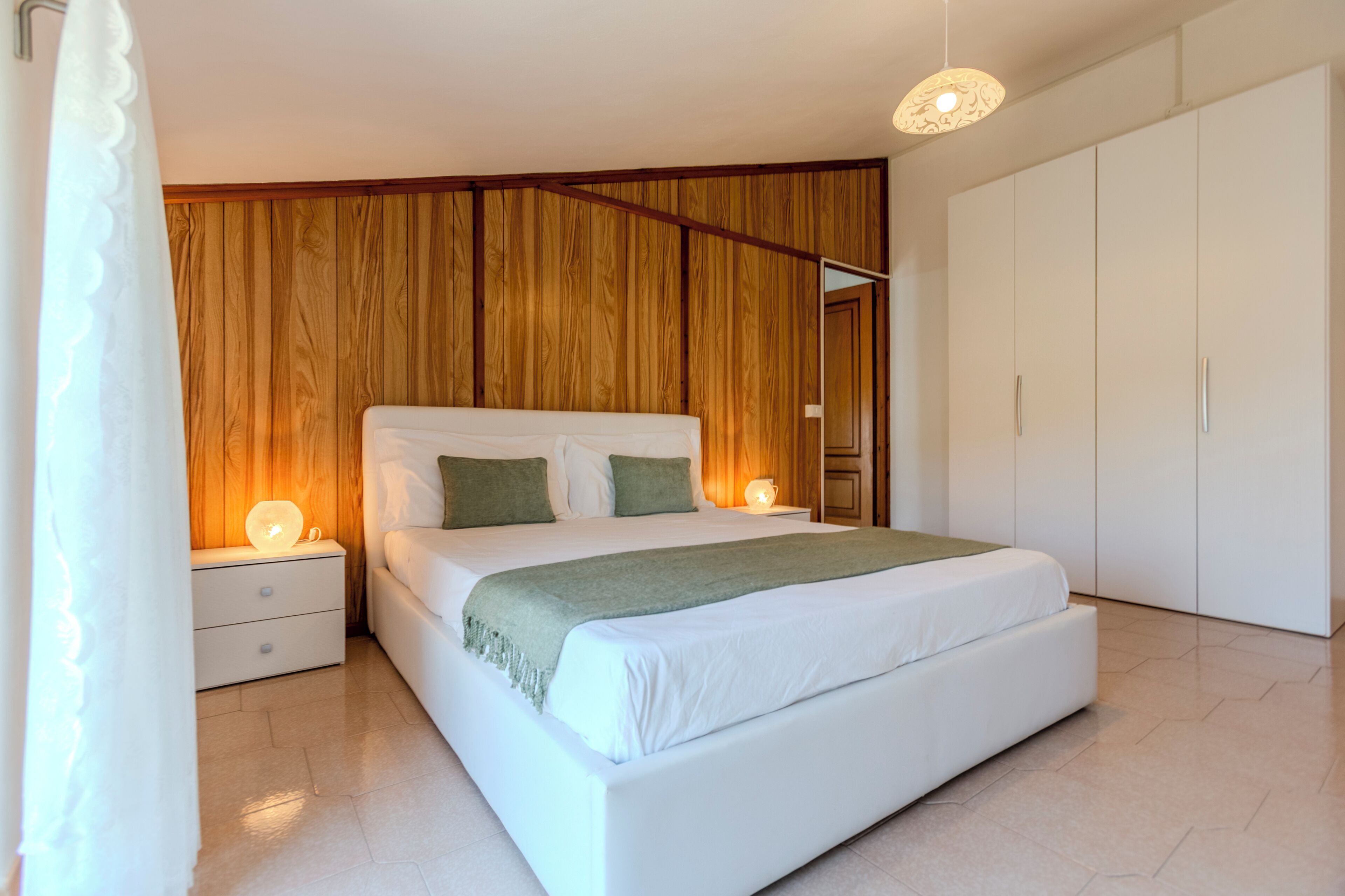Ein Schlafzimmer mit einem Bett, Nachttischen, einem Kleiderschrank und einer Wand mit Holzpaneelen.