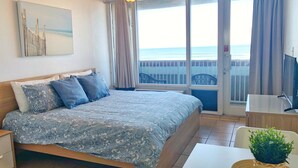 Ein Hotelzimmer mit Bett, Fernseher, Balkon und Meerblick sowie einem Deckenventilator.
