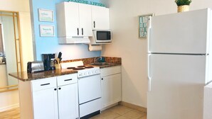 Eine Küche mit weißen Schränken, einem Herd, einer Mikrowelle und einem Kühlschrank. An der Wand hängen gerahmte Bilder und ein Schild mit der Aufschrift 'Seaside Living'.