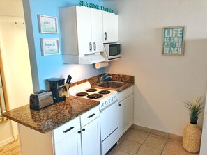 A kitchen with white cabinets, a microwave, a stove, a sink, and a countertop.